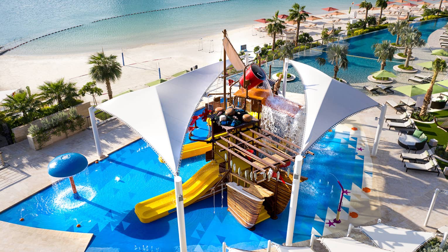 A large orange waterslide built into a faux pirate ship descending into a crystal blue pool of water.