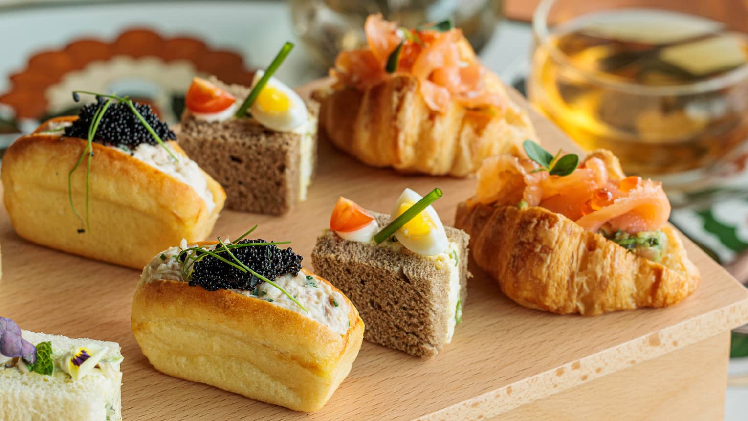 A mini croissant stuffed with salmon, two sandwich cubes and a stuffed bun lined up on a wooden box display