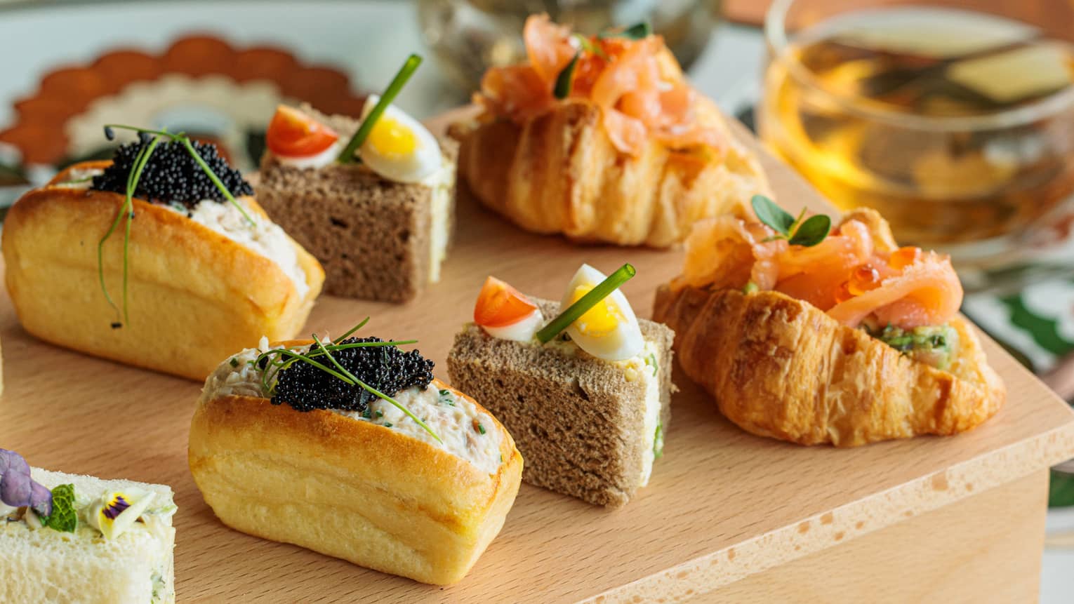 A mini croissant stuffed with salmon, two sandwich cubes and a stuffed bun lined up on a wooden box display