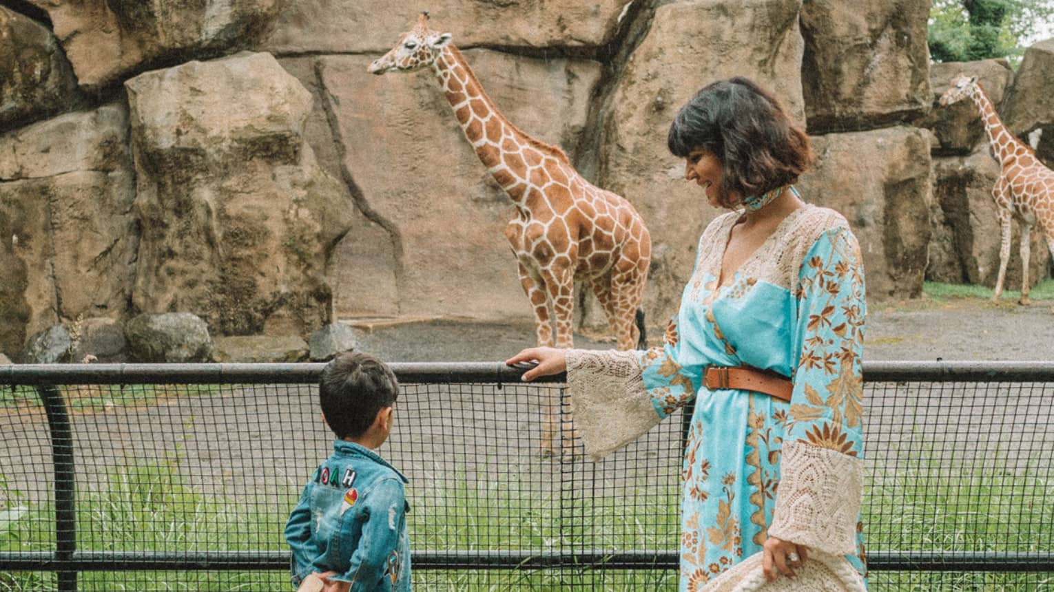A mother with her son looking at giraffes in a zoo.