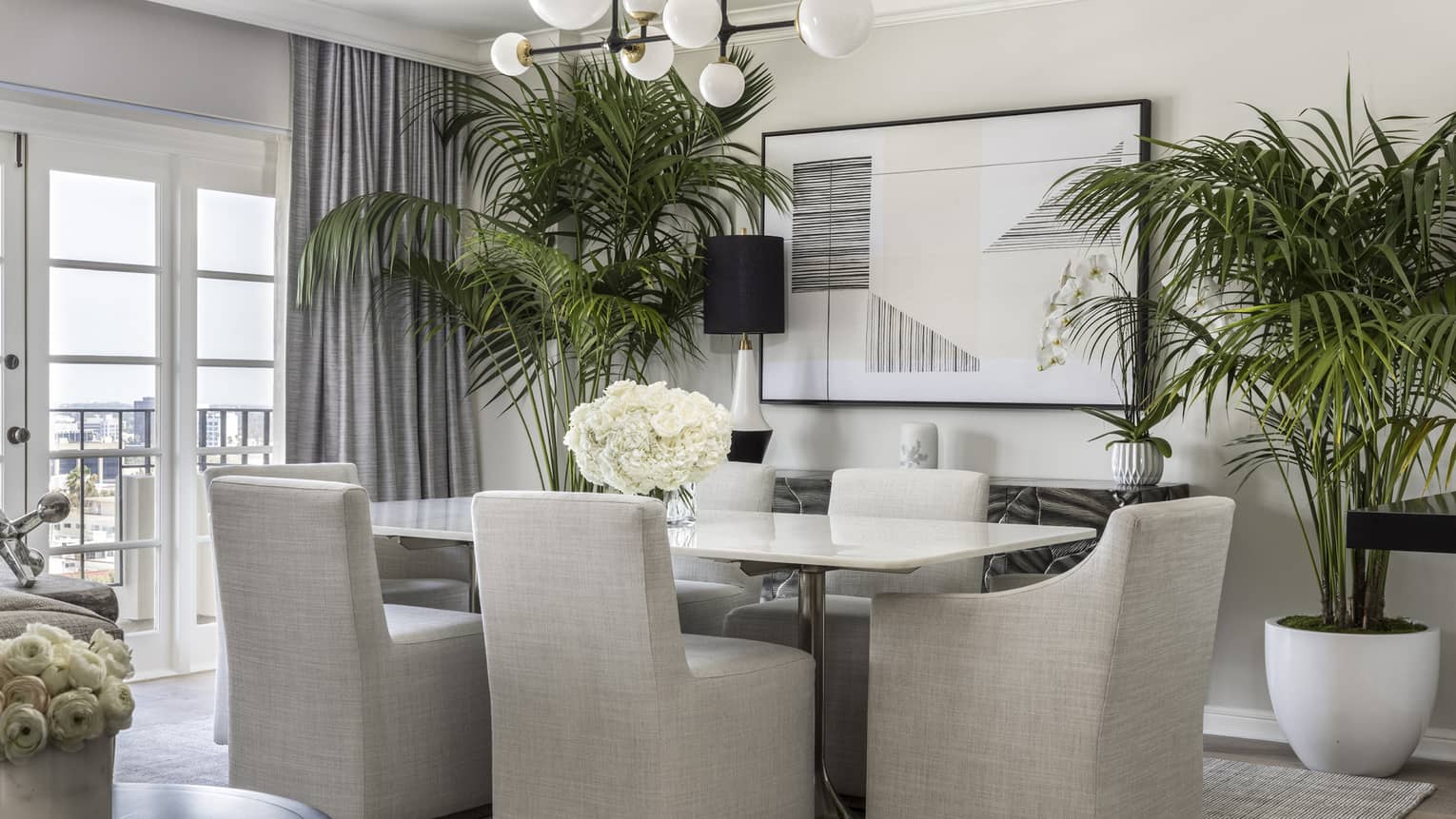 Dining room with white table, four taupe upholstered chairs, modern lighting