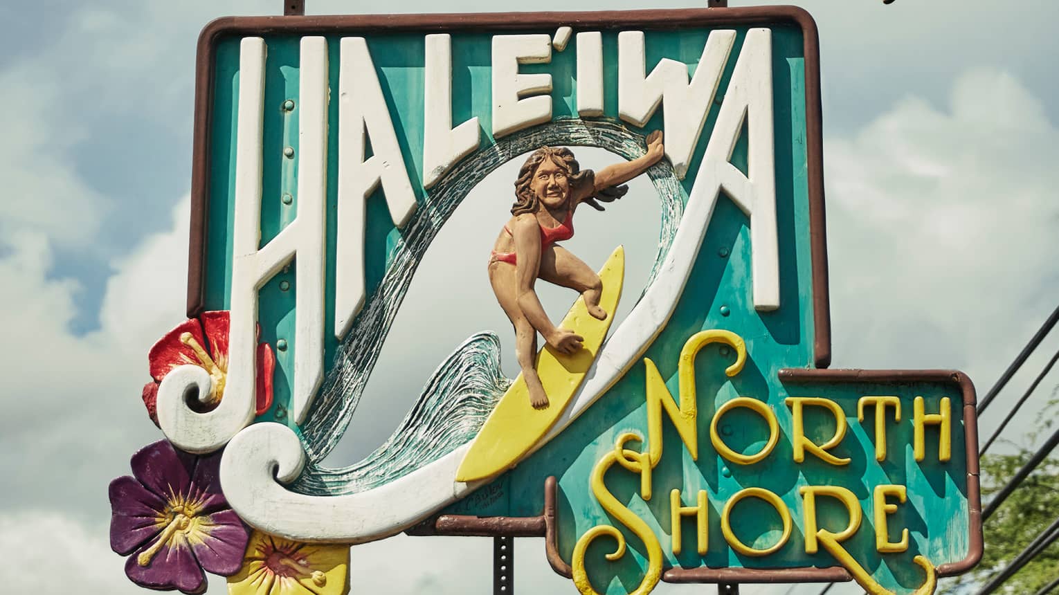 Colourful wood sign reading Haleiwa North Shore with carving of woman on surfboard