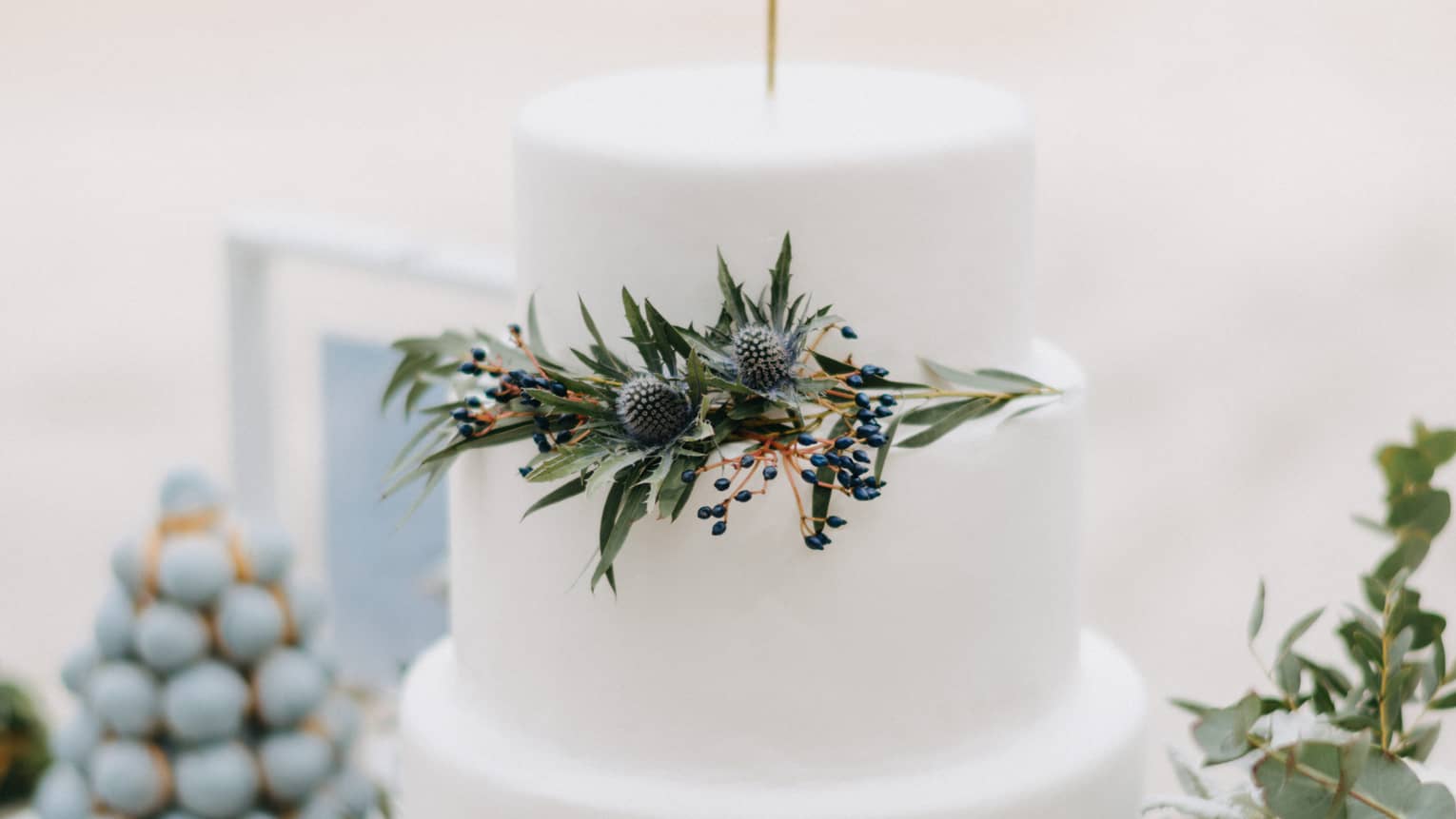 Three tiered wedding cake decorated with green leaves, white flowers