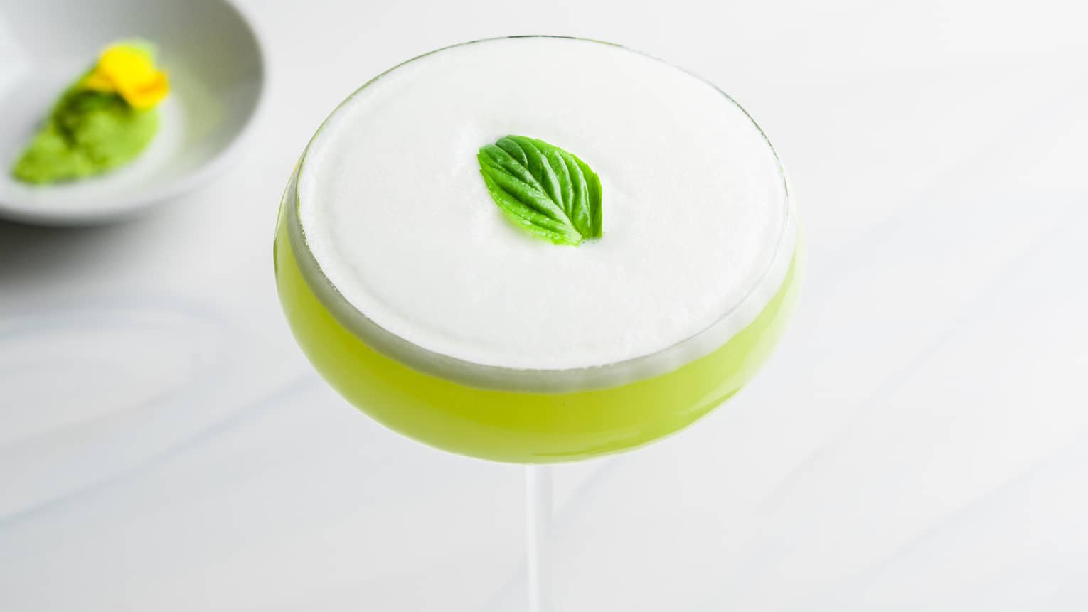 Light Green Wasabi Martini with foamy top and mint garnish in saucer champagne glass