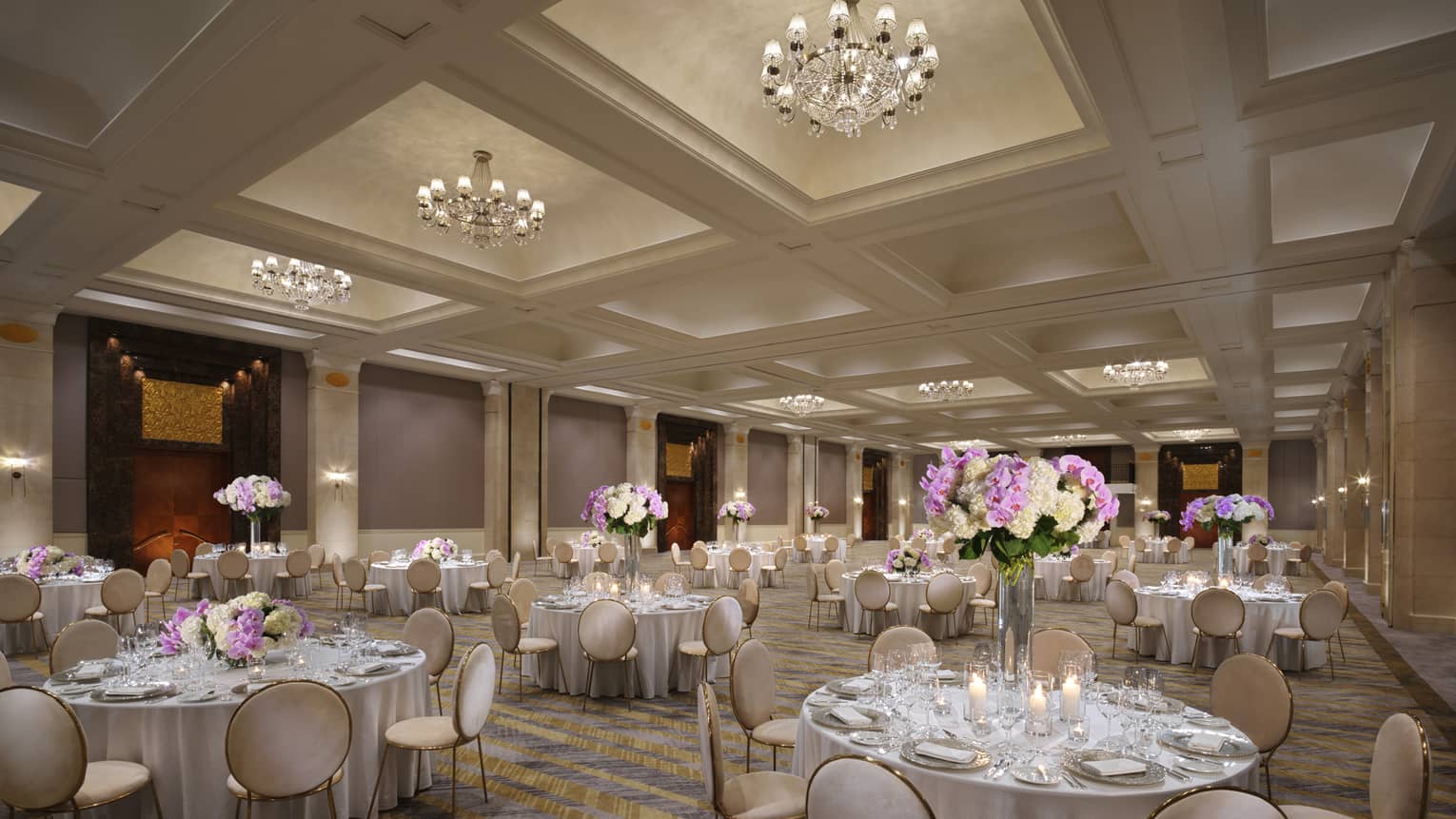 A chandelier-clad ballroom set with several circular tables boasting tall displays of hydrangeas. 
