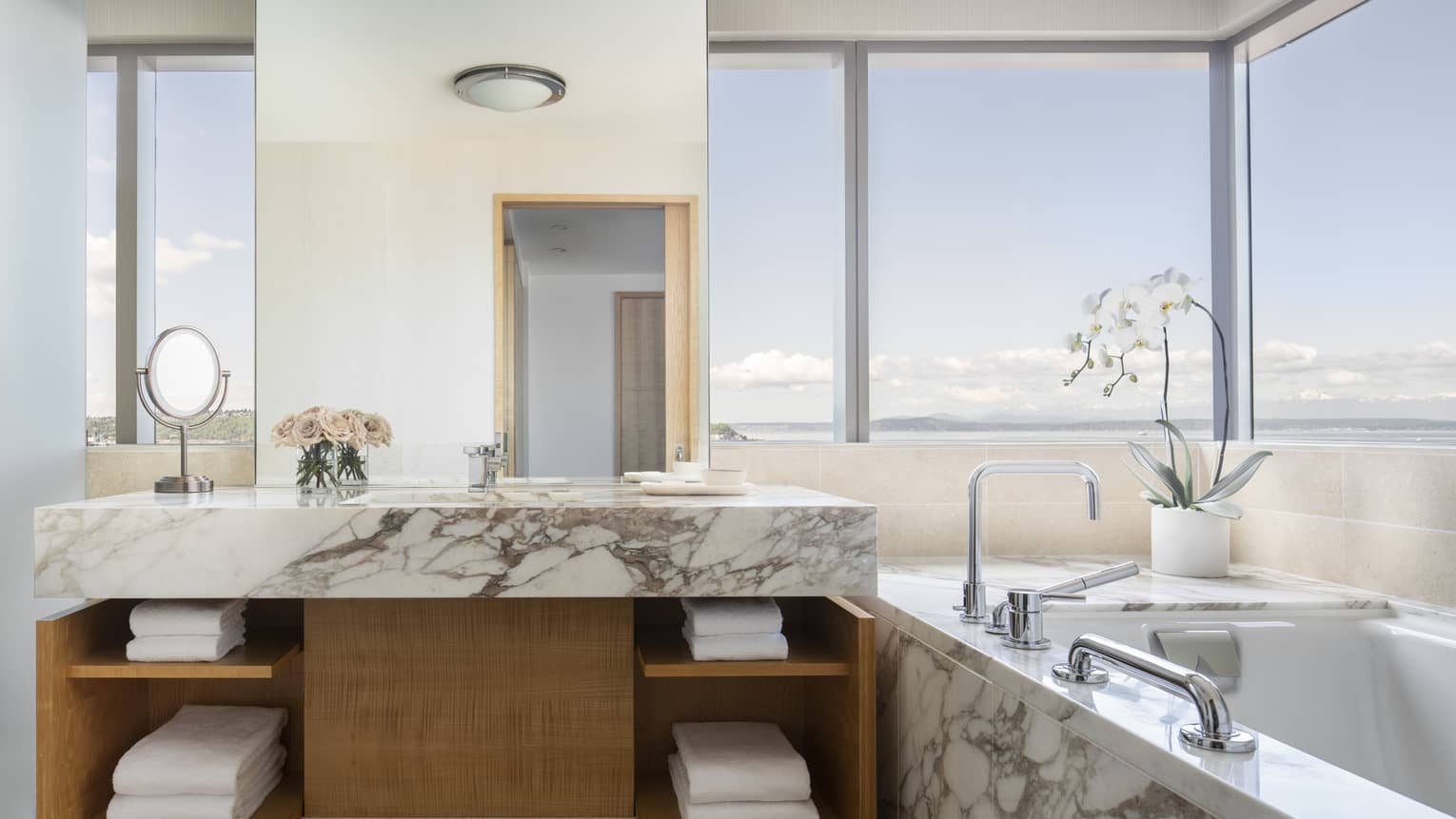 A marble tub and countertops are accented by flowers and multiple windows