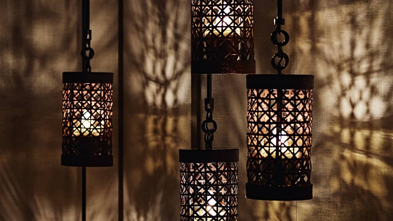 Close-up of black lanterns hanging from chains, light reflected on walls