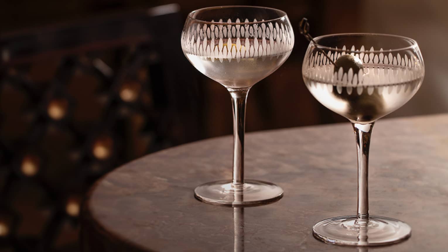 ,Two martinis sit on the edge of a black tabletop