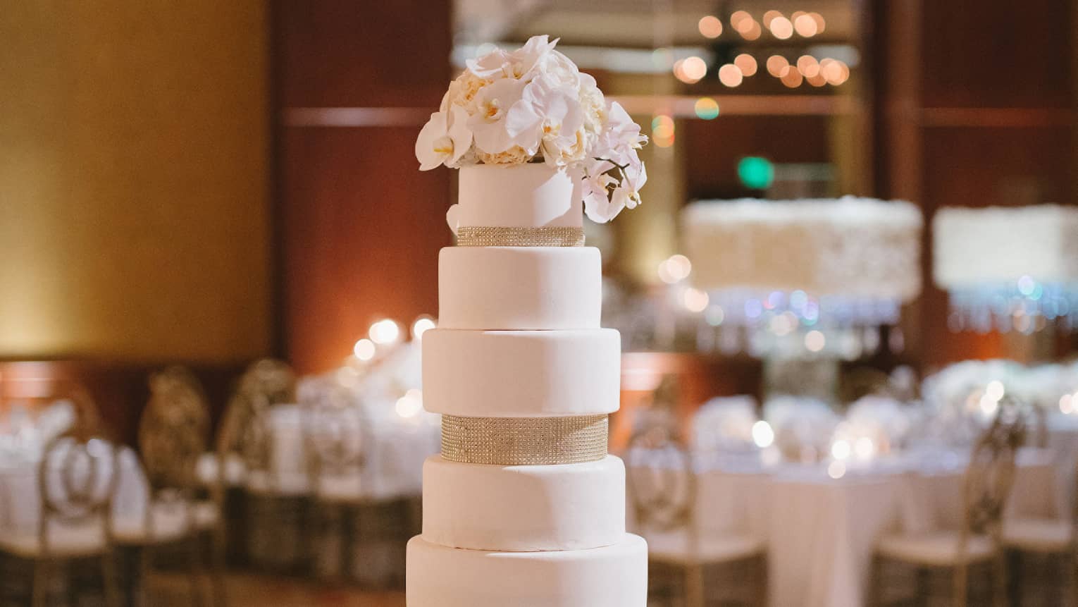 Tall tiered wedding cake decorated with white roses at top, base