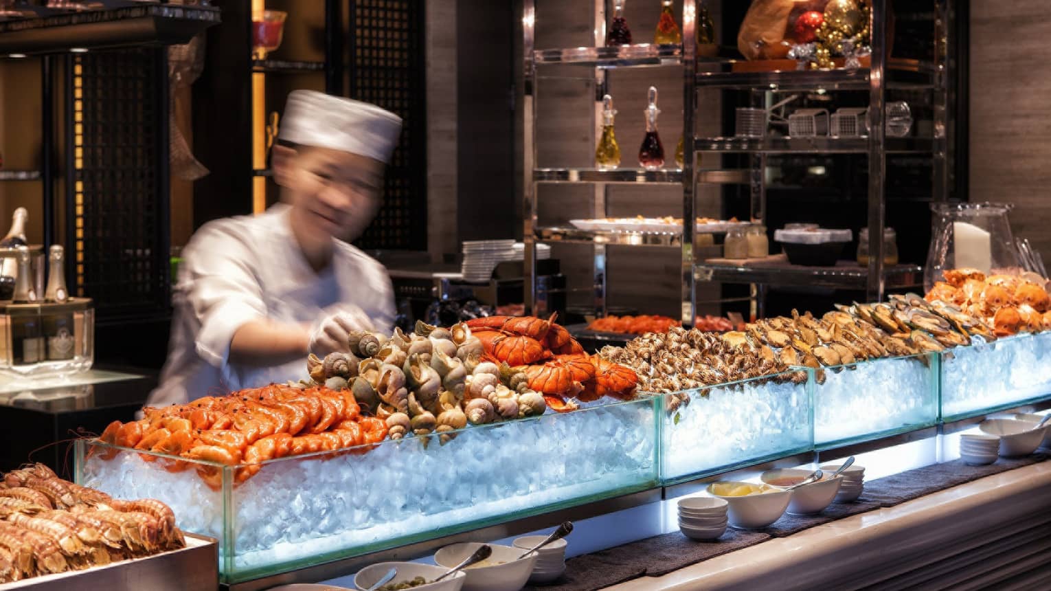 Chef reaches for snails on fresh seafood display on ice at bar 