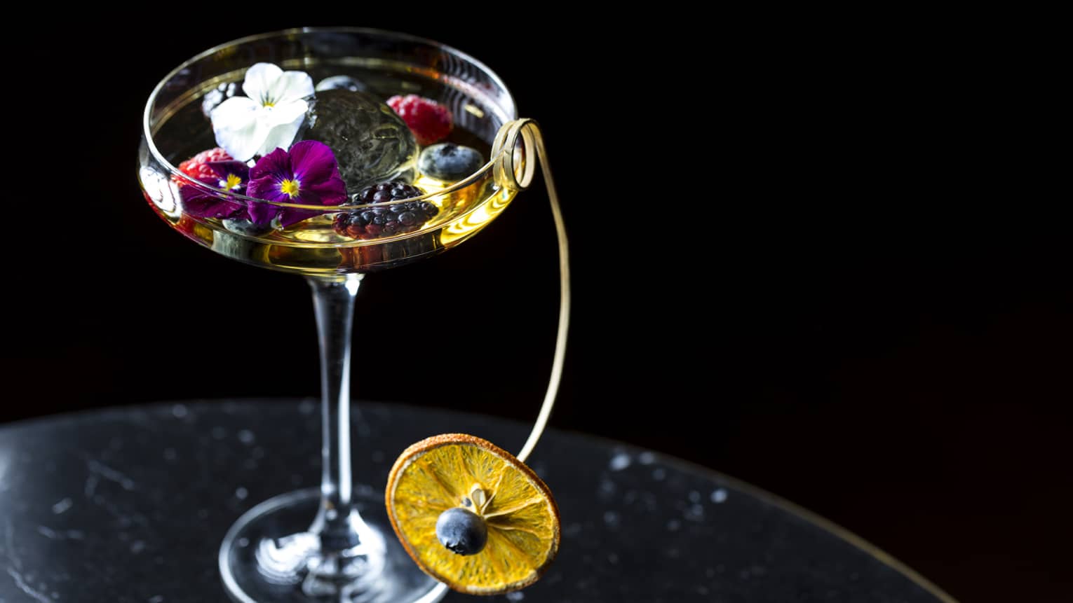 Cocktail glass. liquor garnished with small flowers, berries and dried orange wheel