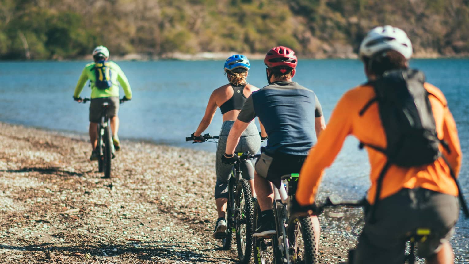 Four people riding bicycles through a rocky terrain next to the ocean