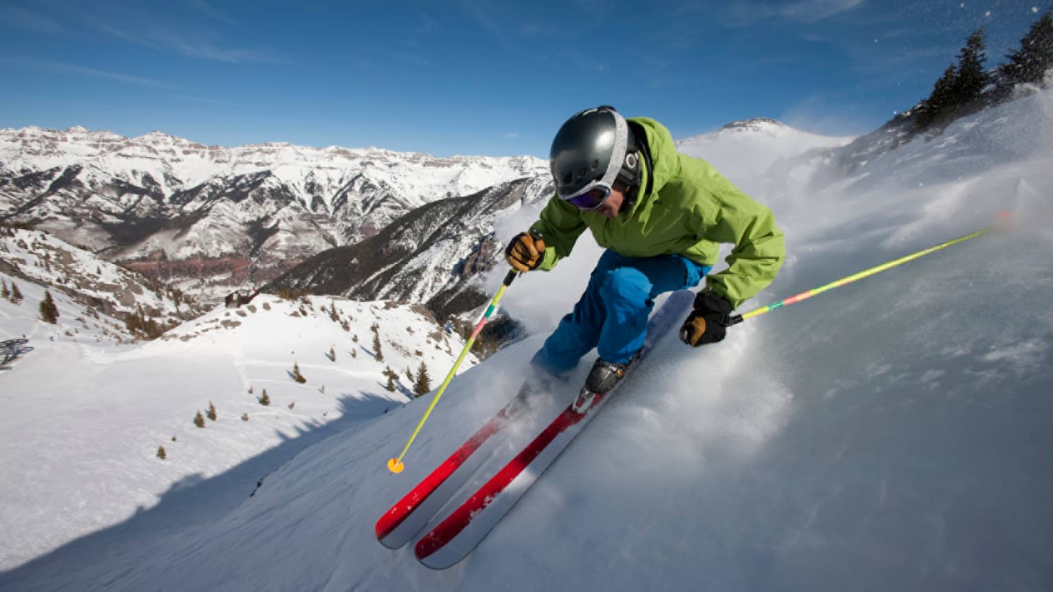 Man in colourful ski jacket, helmet, holds poles, skis down Rocky Mountain