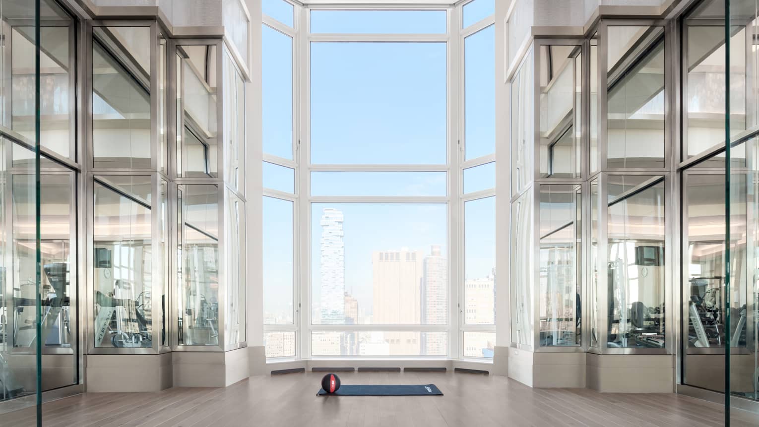 Basketball sits on yoga mat under soaring windows in modern Residential Fitness Centre overlooking Manhattan 