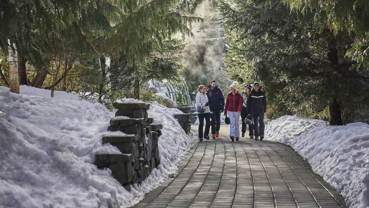 A family walks along a cleared brick path lined with evergreens and a ground filled with snow