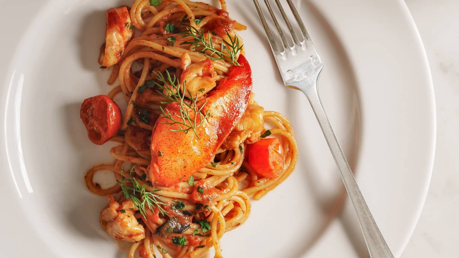 Pasta dish with cherry tomatoes and lobster on round white plate