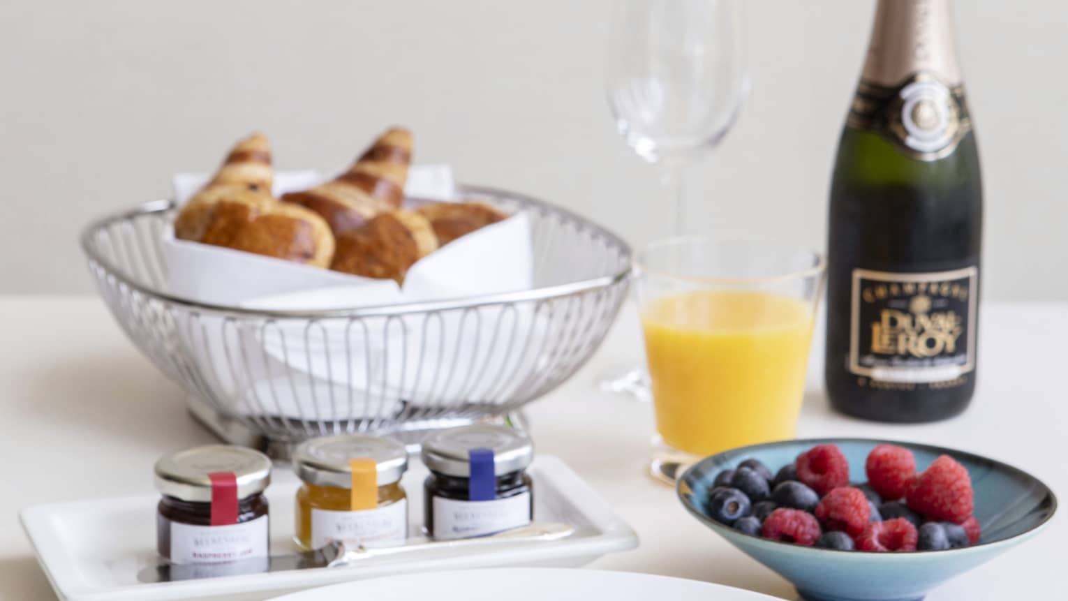 Luxurious breakfast including avocado toast, a basket of croissants, fresh fruit, and champagne and orange juice.