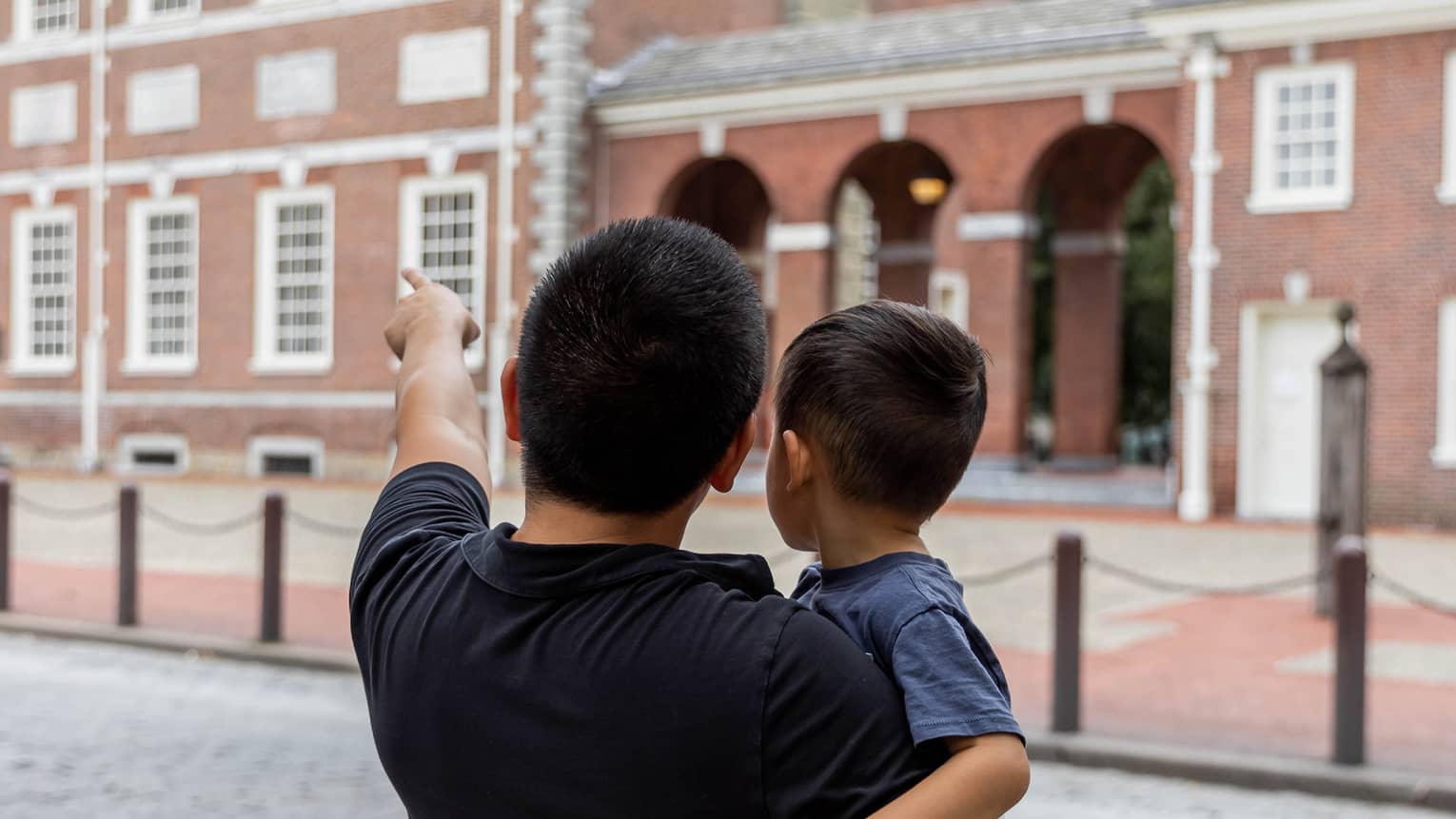 A man holding a boy and pointing at an old brick building.