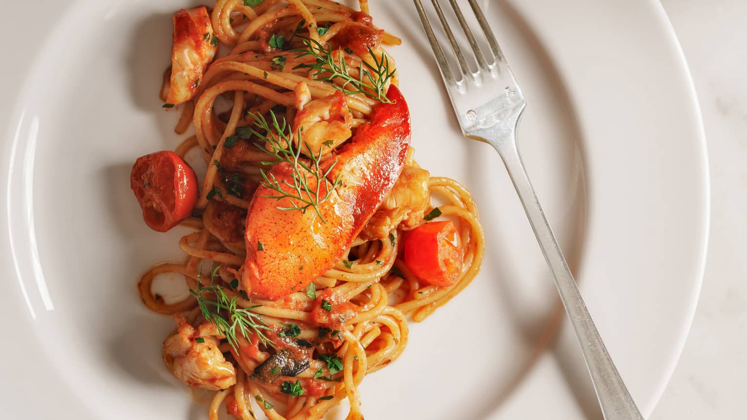 Pasta dish with cherry tomatoes and lobster on round white plate