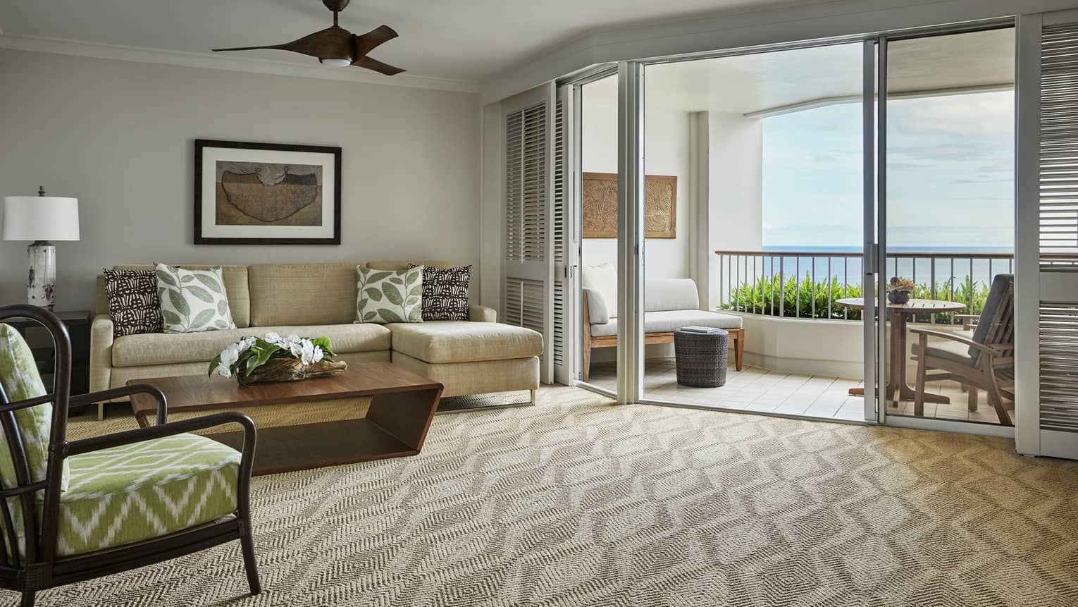 Oceanfront Suite living room with L-shaped sofa, chair on carpet, shutters on patio door