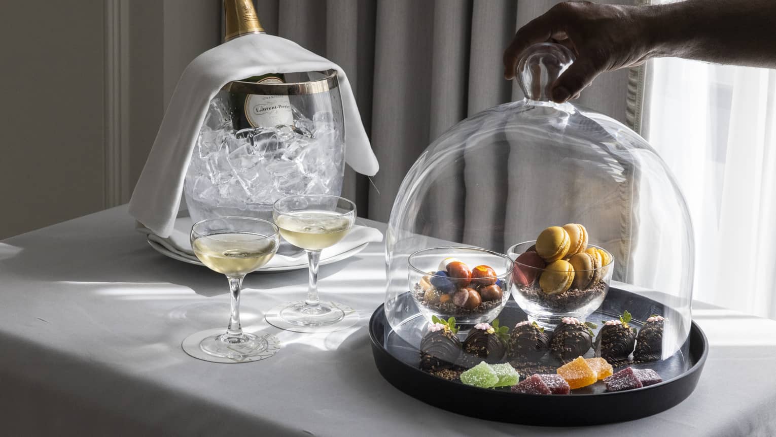 Sweets under a glass dome next to wine.