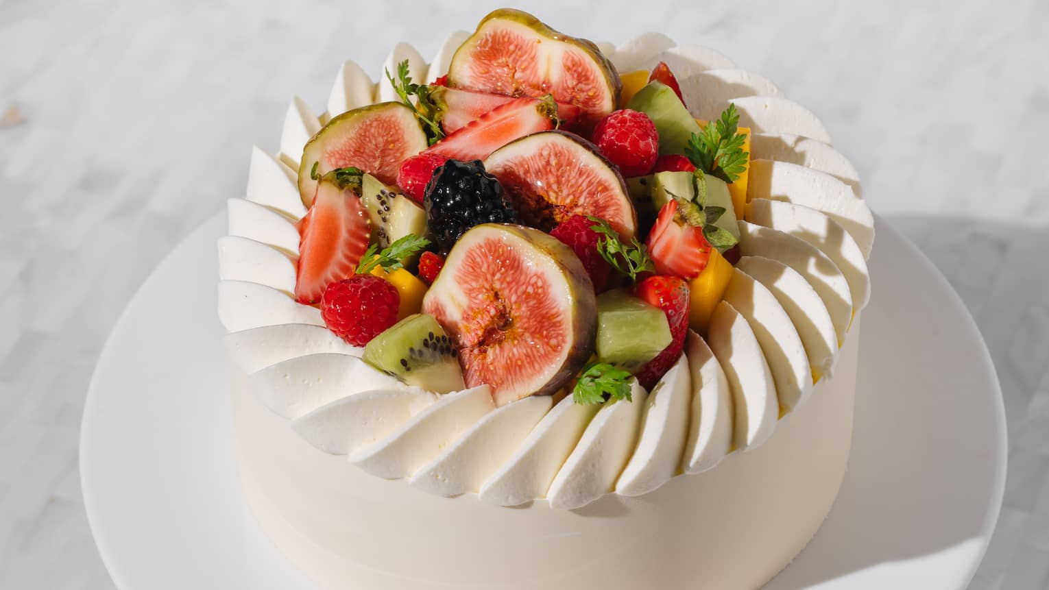 Round white cake on pedestal with fresh figs, kiwi and strawberries