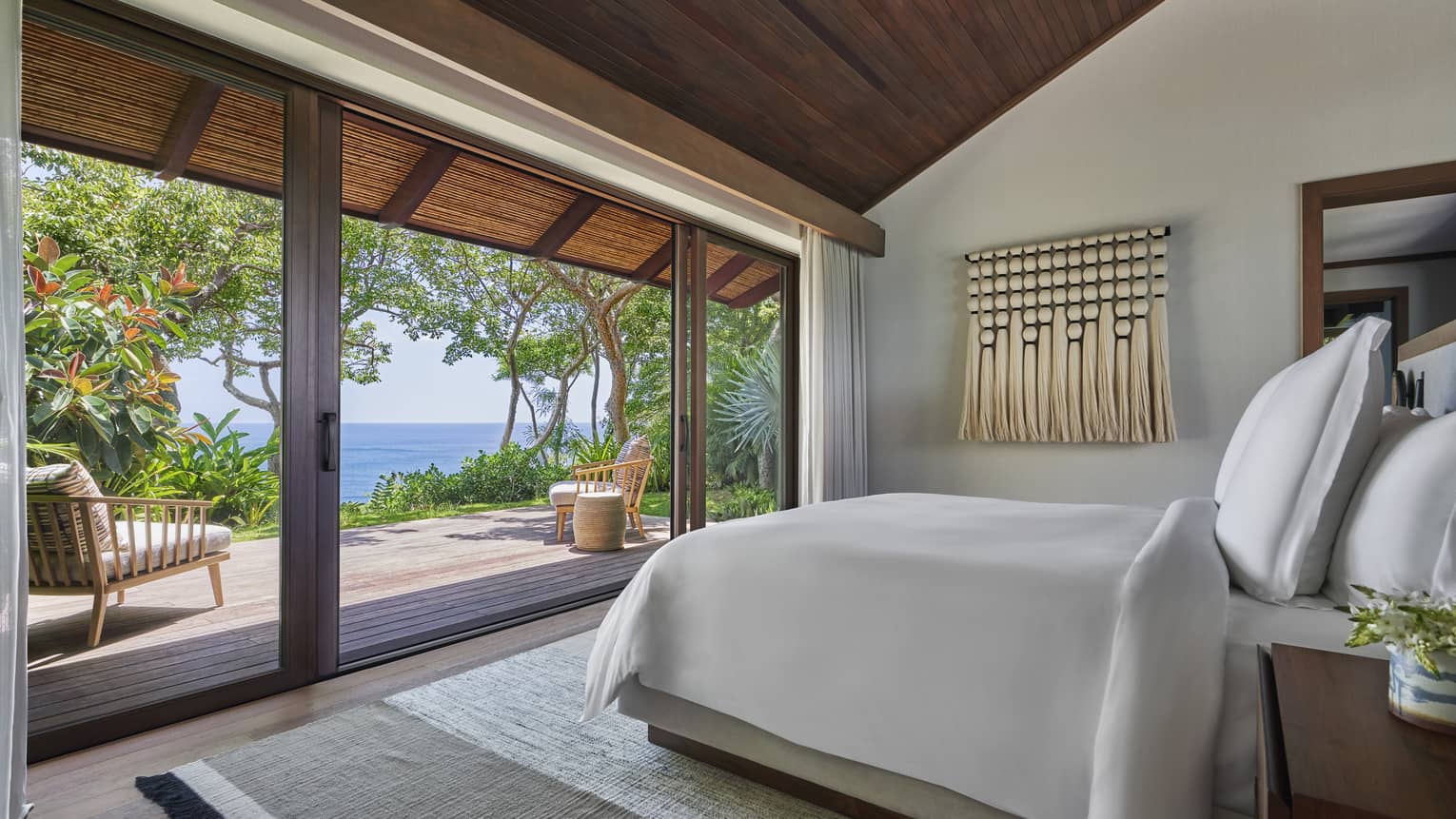 Bedroom with king bed, facing sliding doors that lead out to a private terrace with garden and sea views