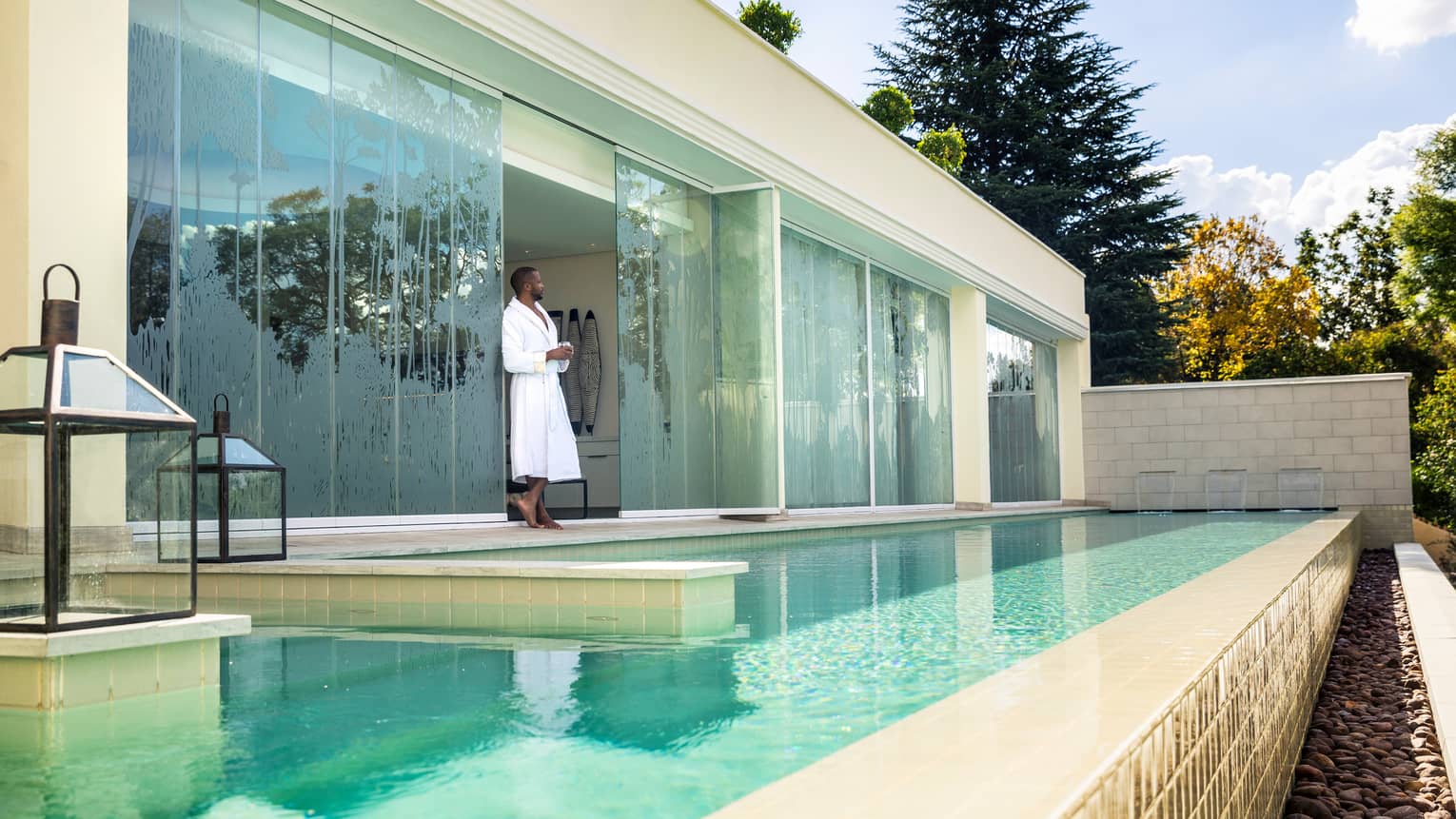 Man in white bathrobe stands between Spa glass windows on swimming pool deck