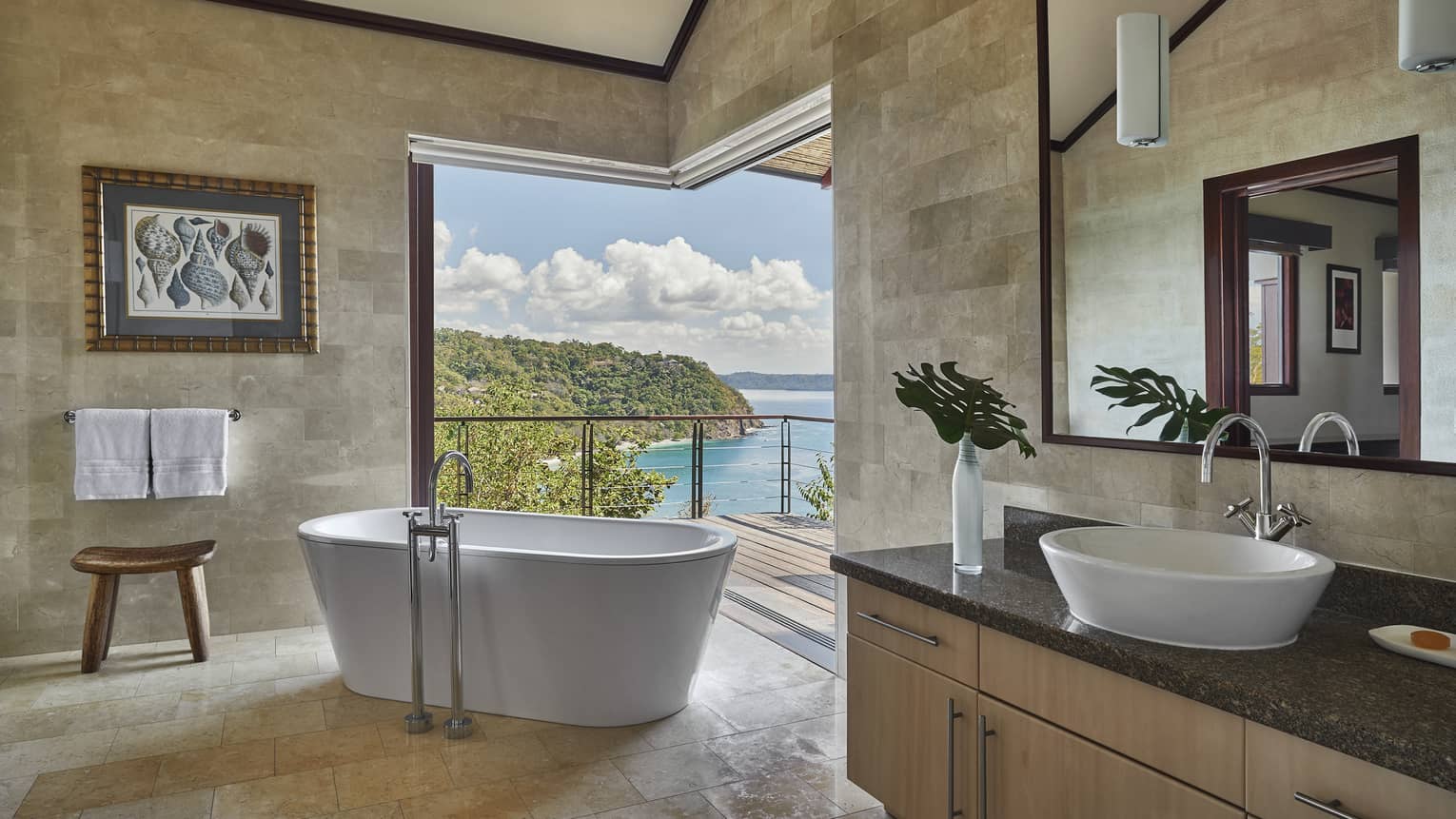 A large oval tub sits at the entrance of a spacious balcony overlooking the ocean.
