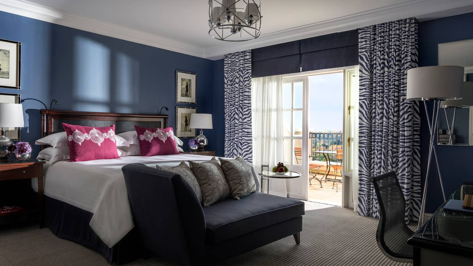 Hotel room with navy walls, white bed and magenta pillows, black settee at foot, zebra curtains by french doors