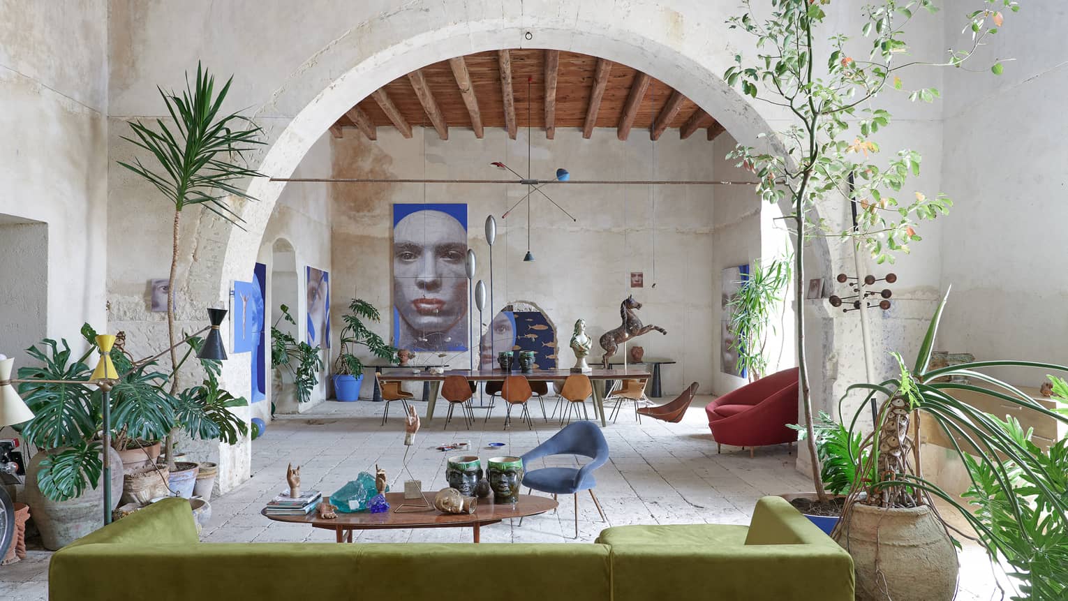 Large room with tropical plants, contemporary furnishings, an arched stone wall and artwork in the distance