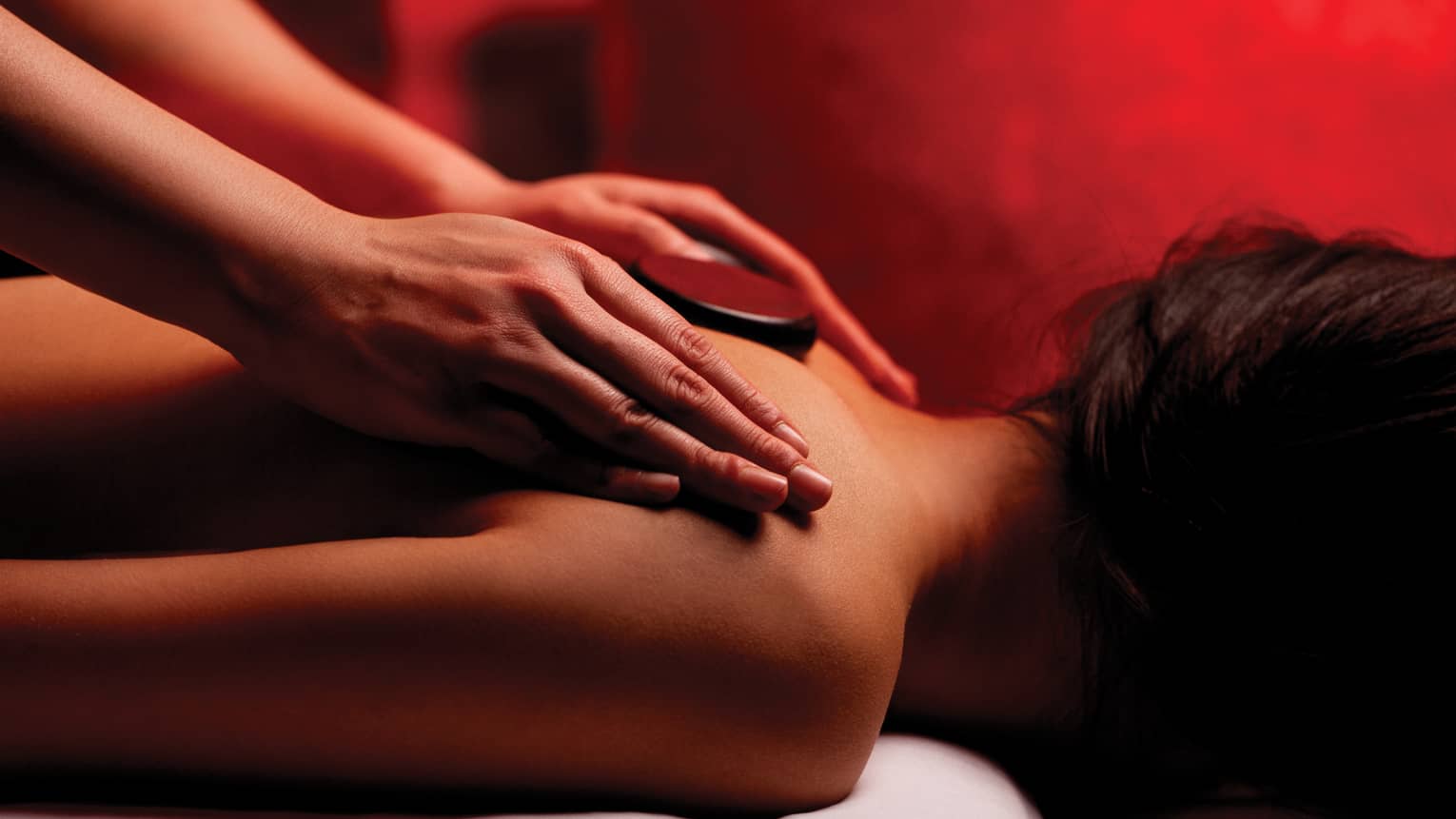 Hands rub woman's bare shoulders during Fusion Massage in spa