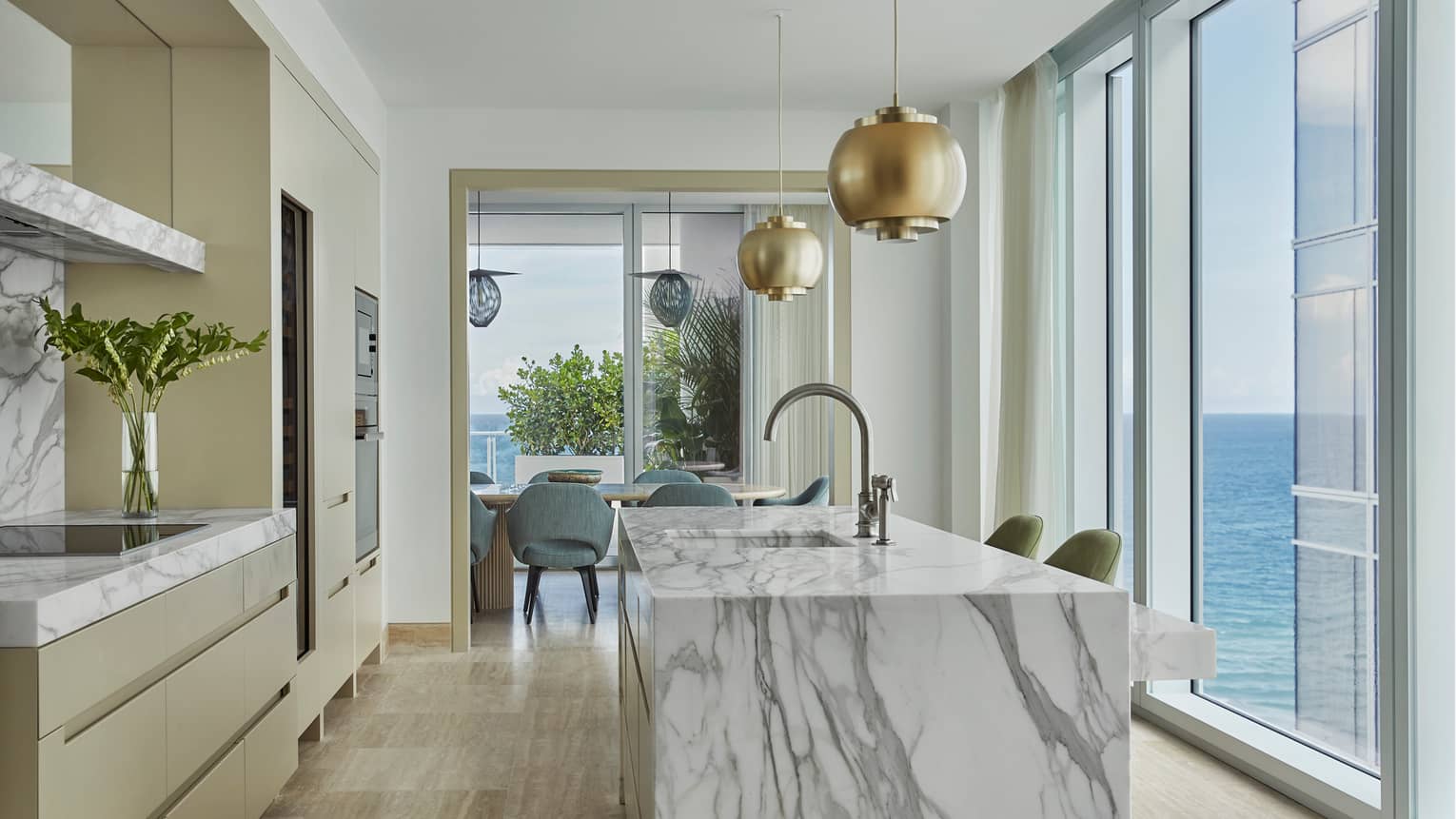 Retro-style brass lamps above grey marble kitchen island, glass wall with ocean views