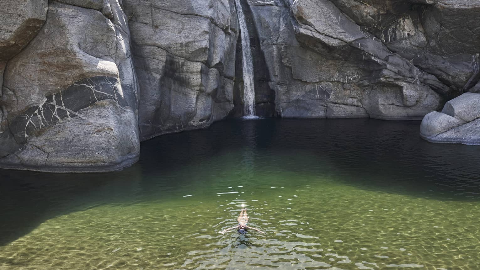A person in a small well of water surrounded by large rock faces and trees.