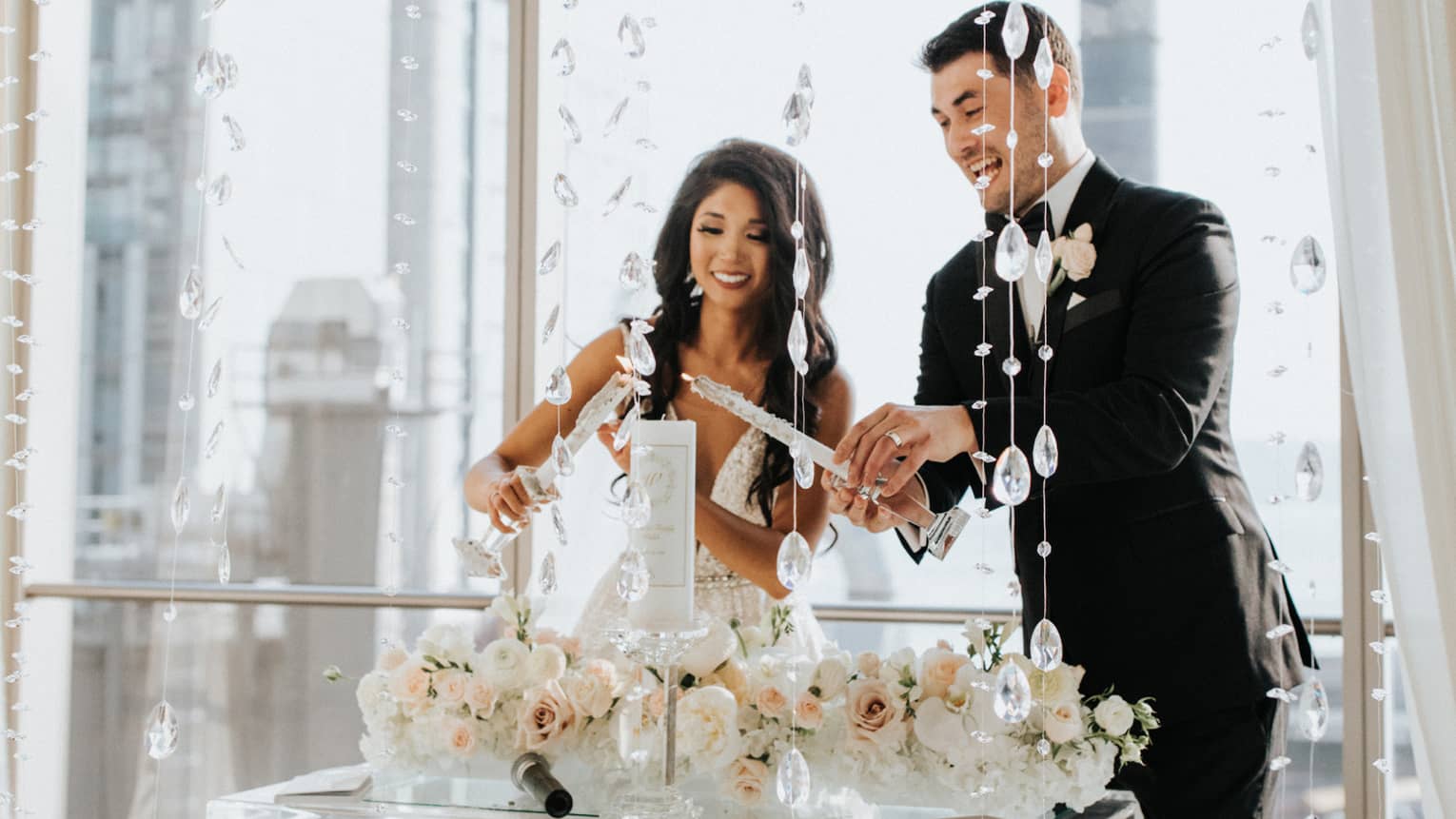 Bride and groom light wedding candle at glass podium by floor to ceiling window