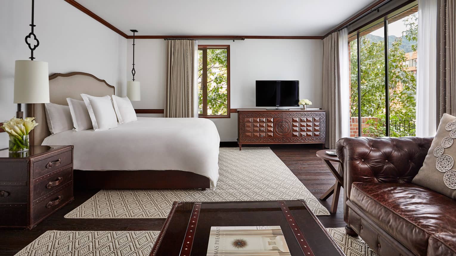 Executive Suite with bed with white linens, wood trunk-style coffee table and nightstand, large glass patio door