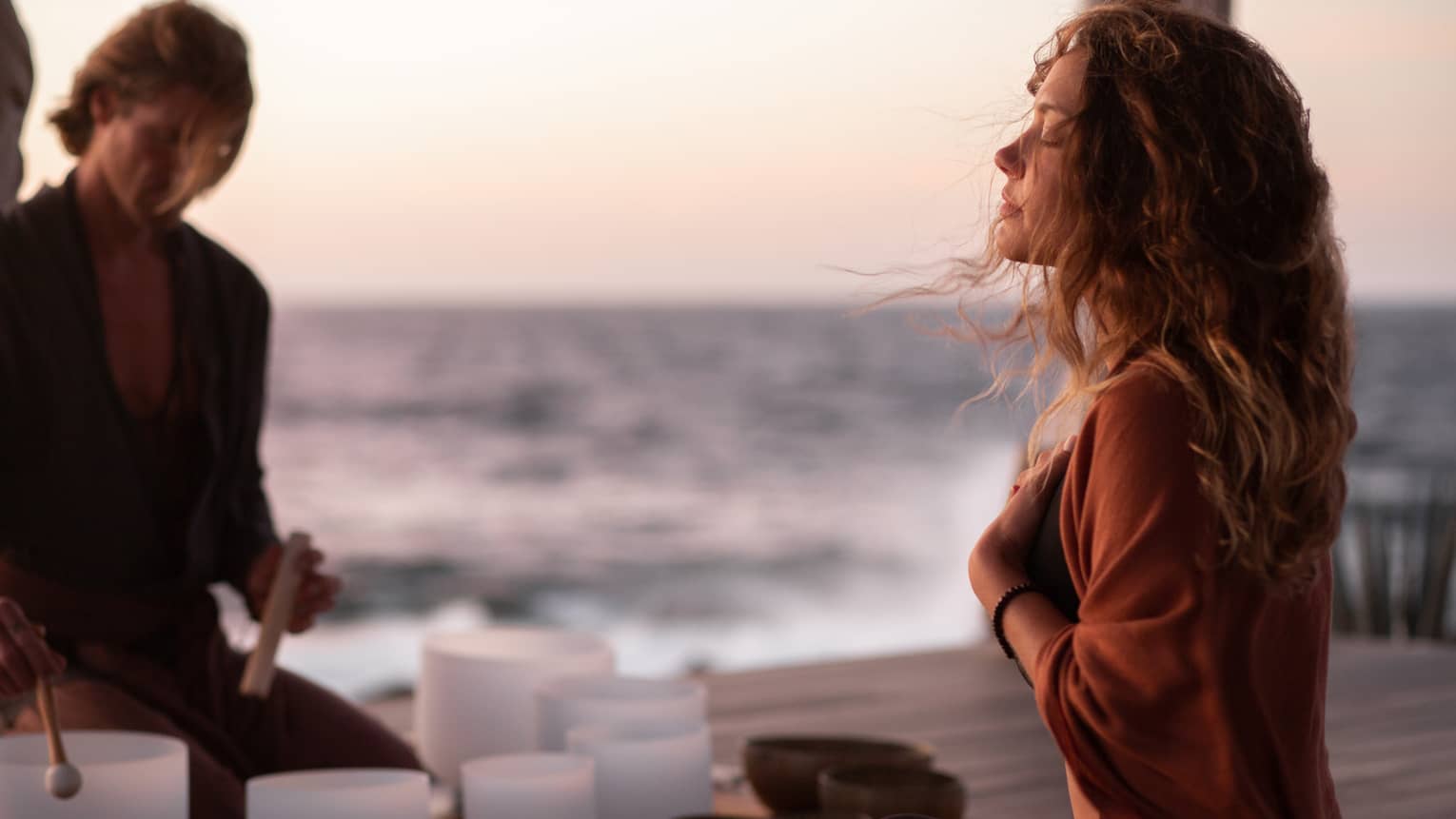 A woman participating in breathwork and sound meditation outside near an ocean.