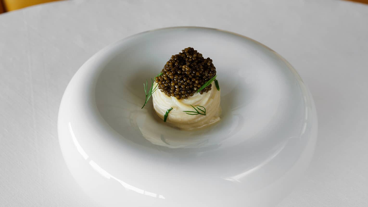 Elegant timbale topped with caviar and garnished with dill sprigs on avant-garde white dish