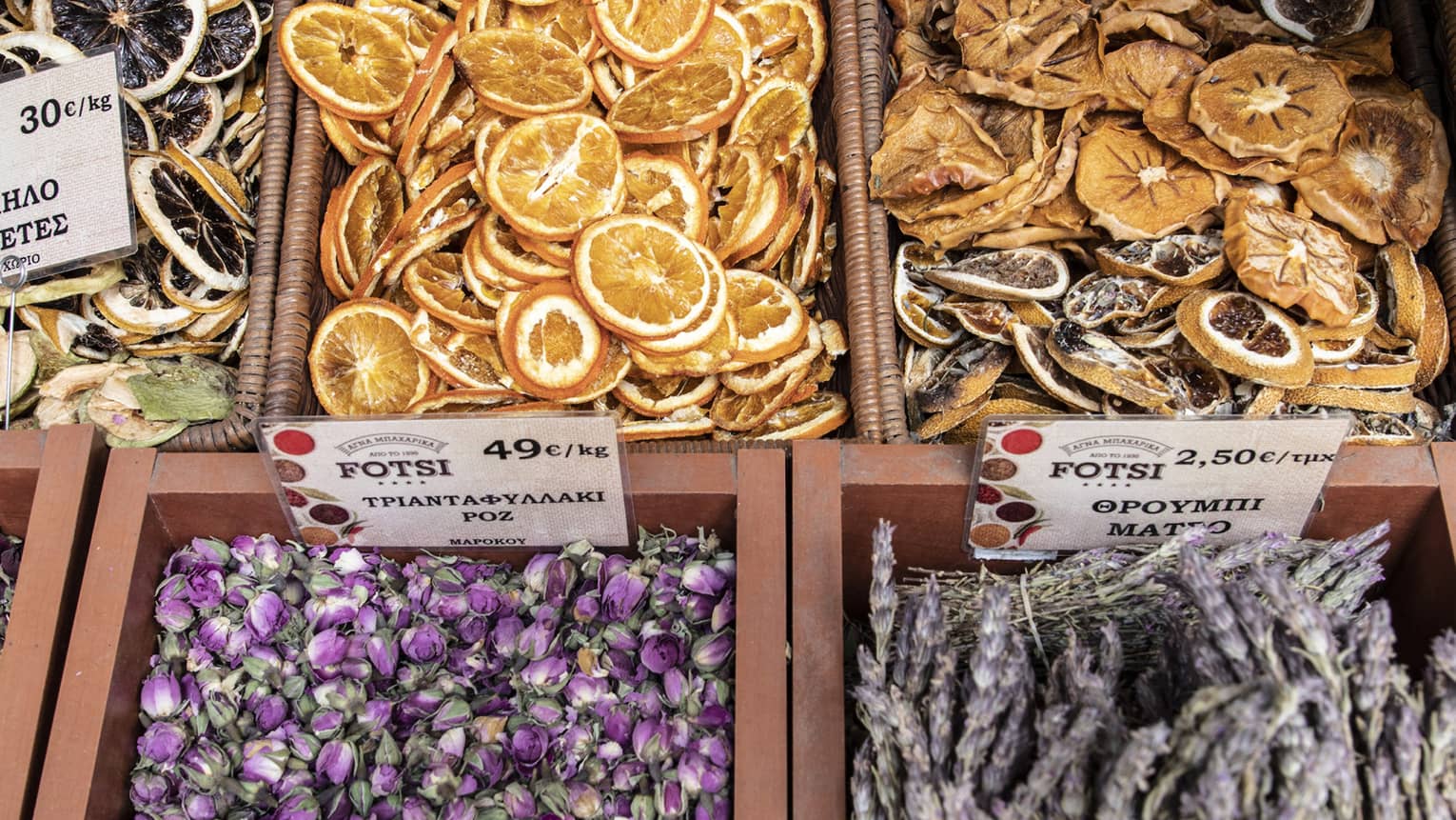 Dried orange slices and purple rose buds, lavender bundles and cinnamon sticks displayed for sale in wooden and wicker boxes.