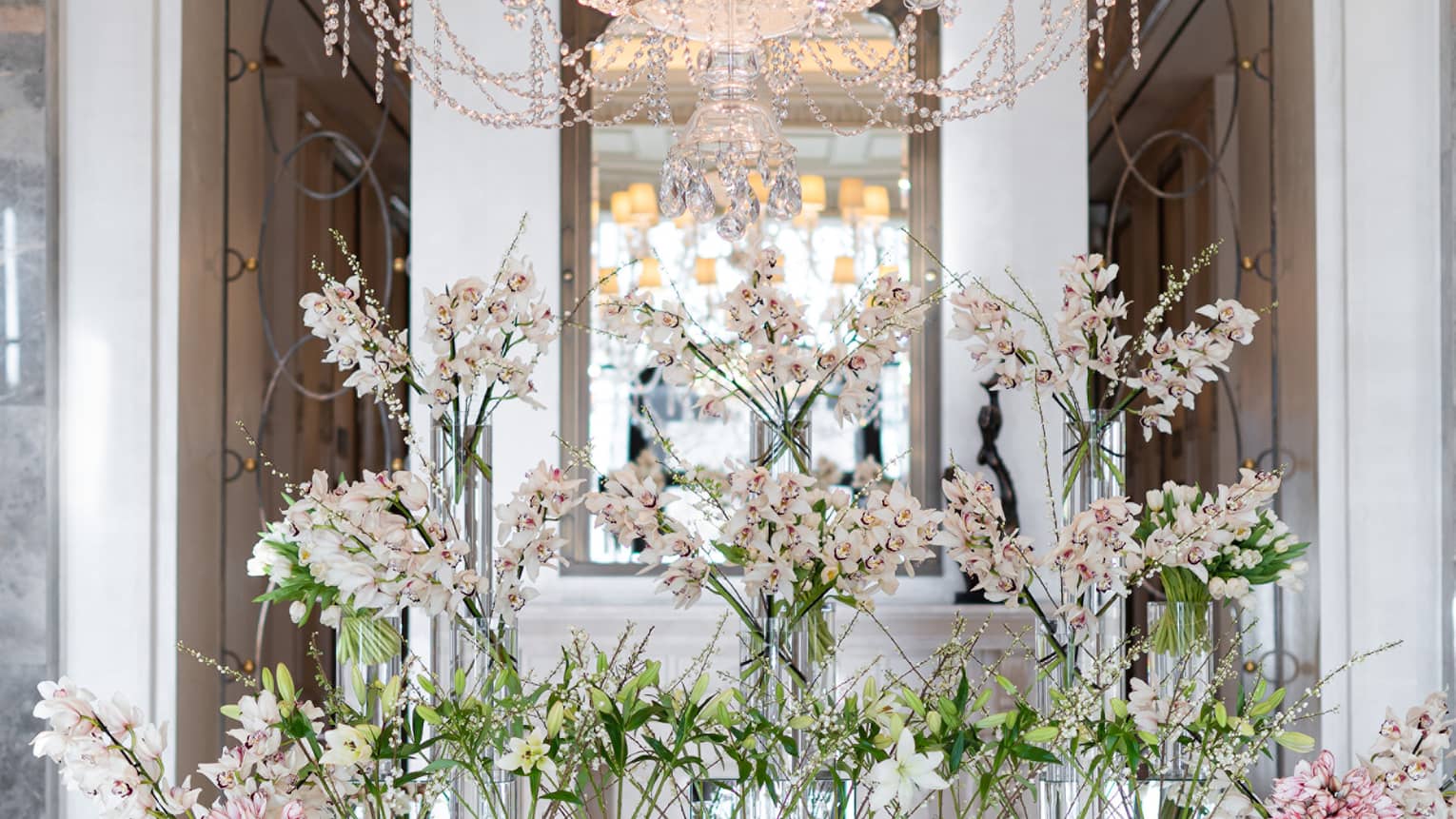 Hotel lobby with large crystal chandelier hanging over floral display in crystal vases