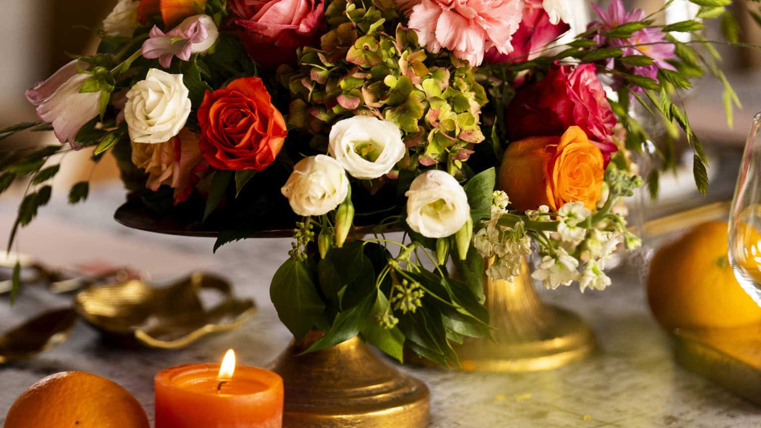 Bouquet of assorted autumn-coloured flowers with burnished pillar candles beside it