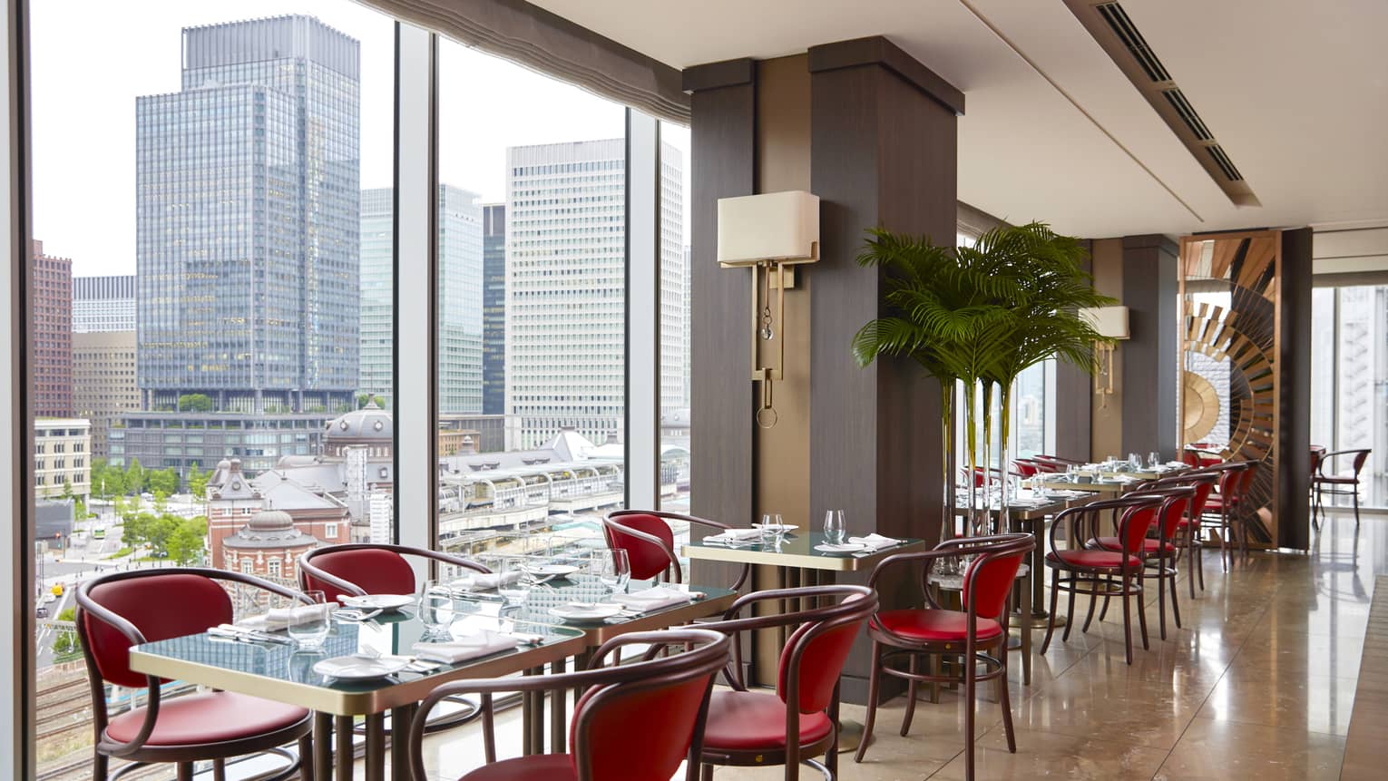 Row of four tables with four chairs each at Maison Marunouchi, floor-to-ceiling windows with views of downtown Tokyo