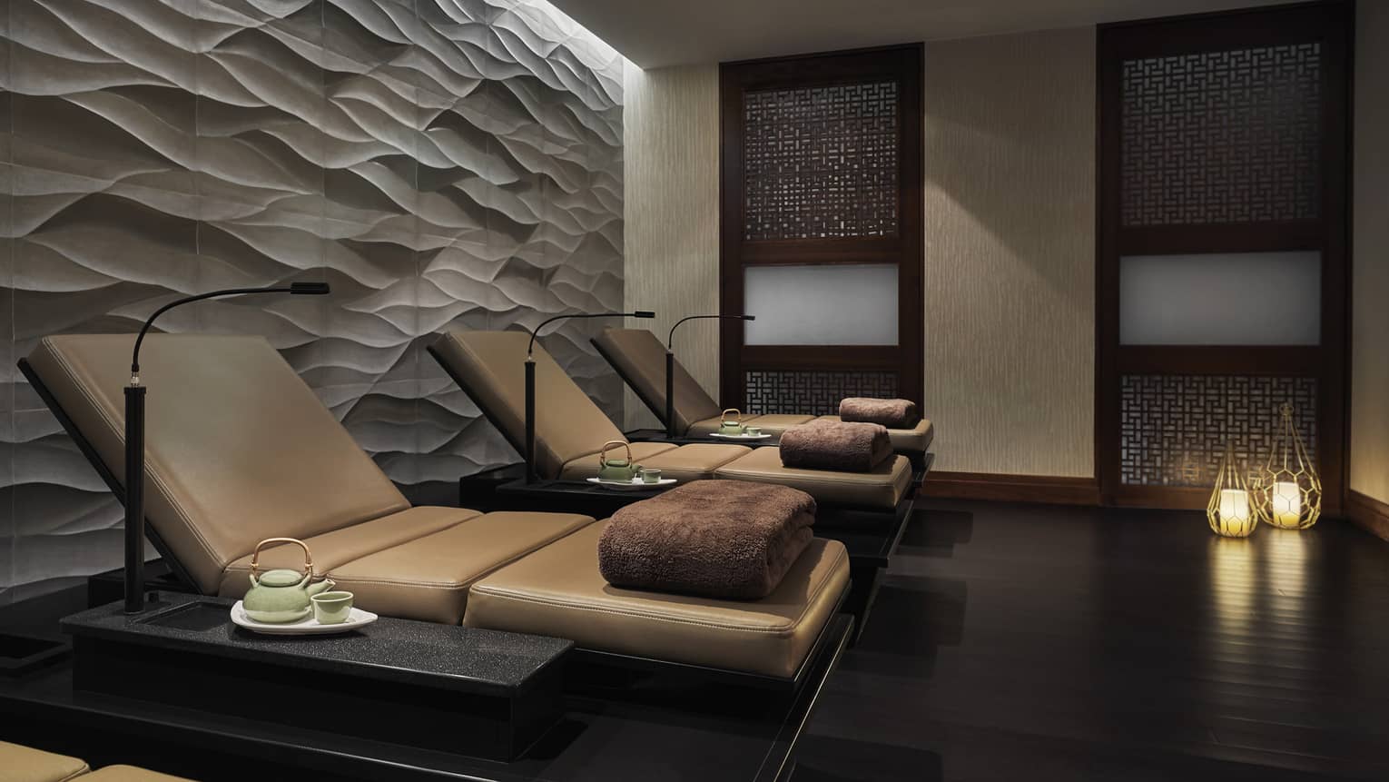 Several lounge chairs with large brown towels placed atop them in a stone room.