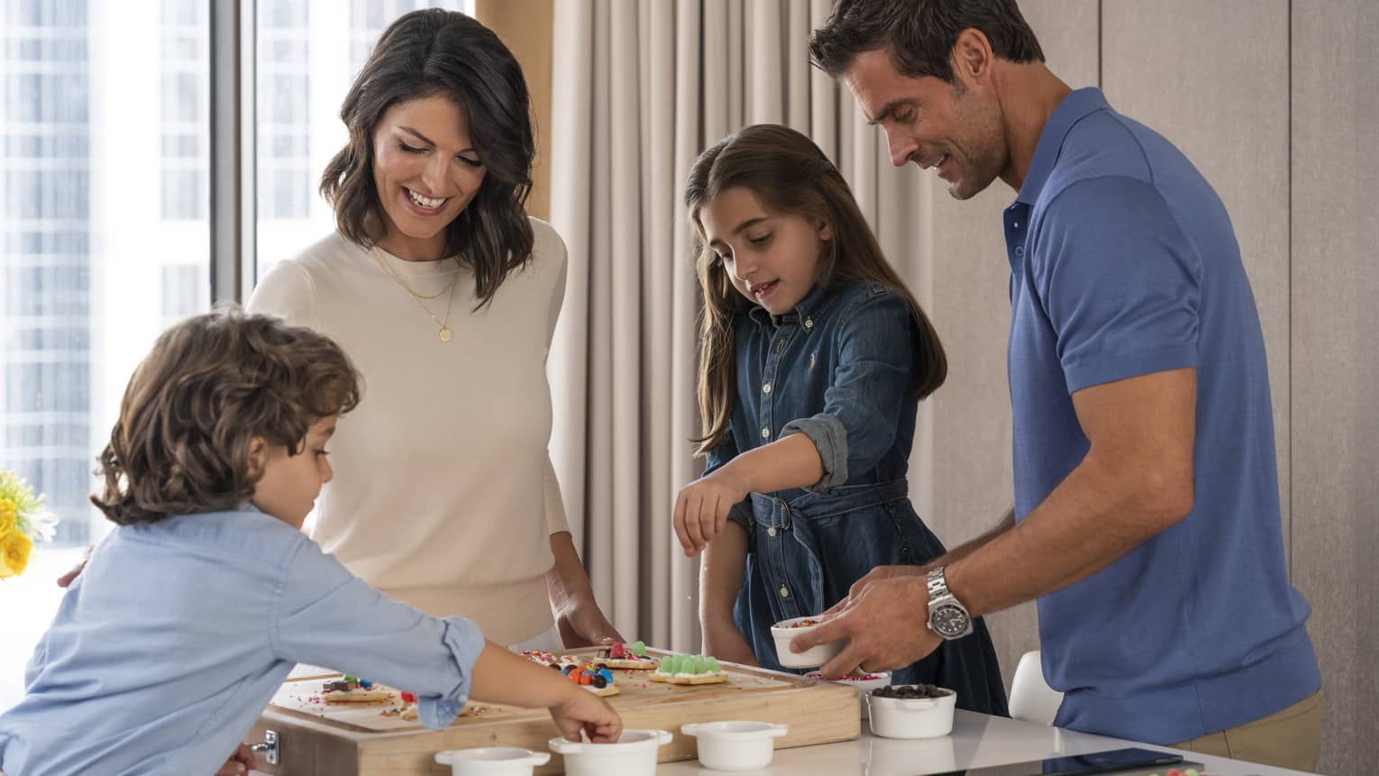 Woman, man, young girl and young boy decorate cookies at kitchen island