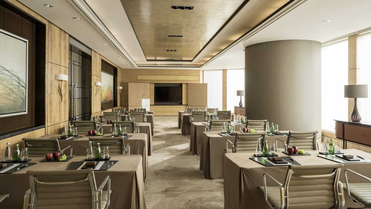 Conference room with rows of small tables, pairs of chairs facing screen, large pillar 