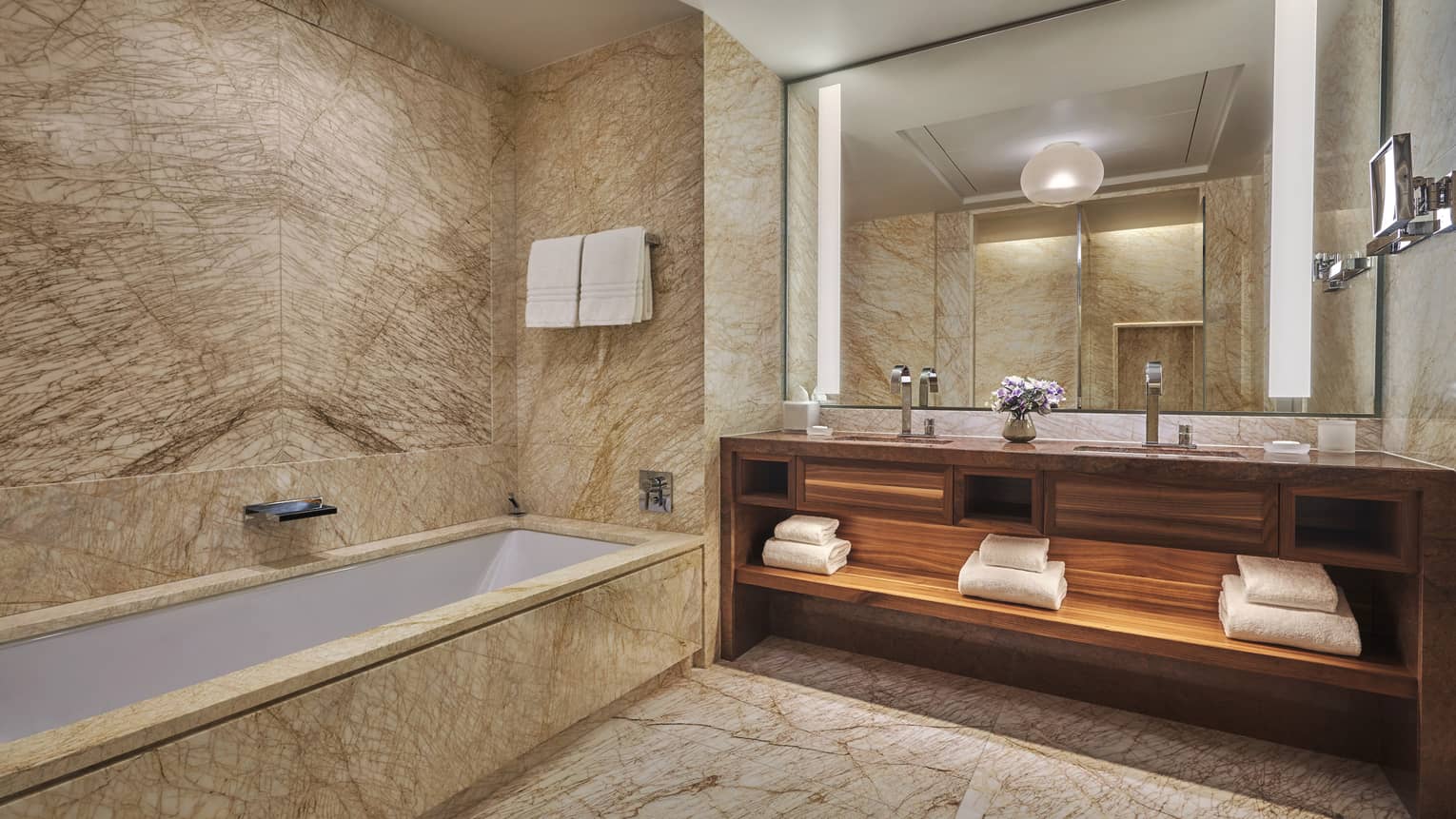 Guest bathroom with rectangular marble tub and floors, double wooden vanity, mirror