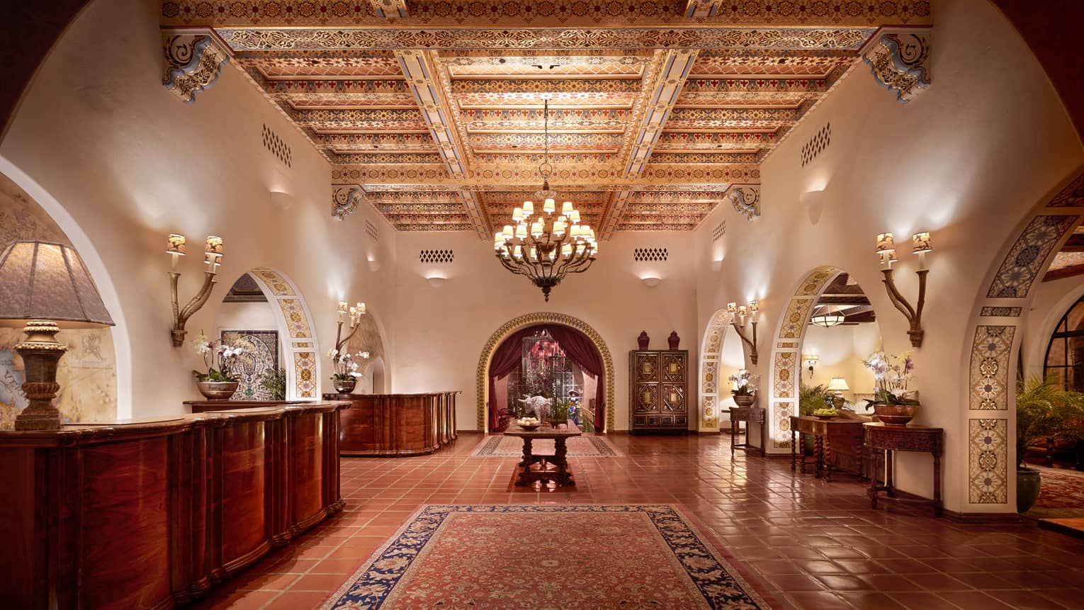 Colourful Spanish tiles covering ceiling, beams above chandelier, area rug, hotel lobby