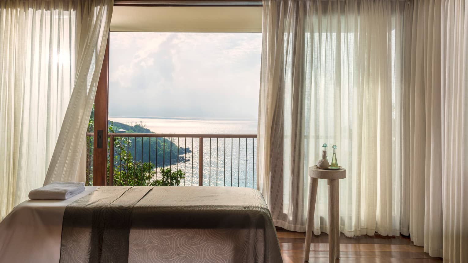 Massage bed in front of open window with long white curtains, ocean view 