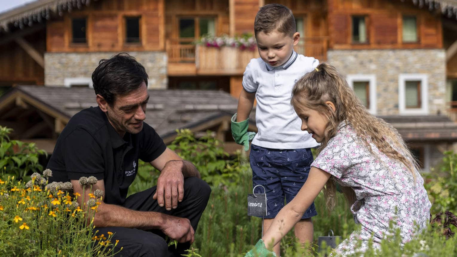 Man kneeling in meadow with two children with chalet in backdrop