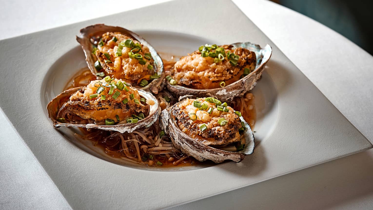 Four oyster shells with Steamed Live Abalone in bowl with sauce